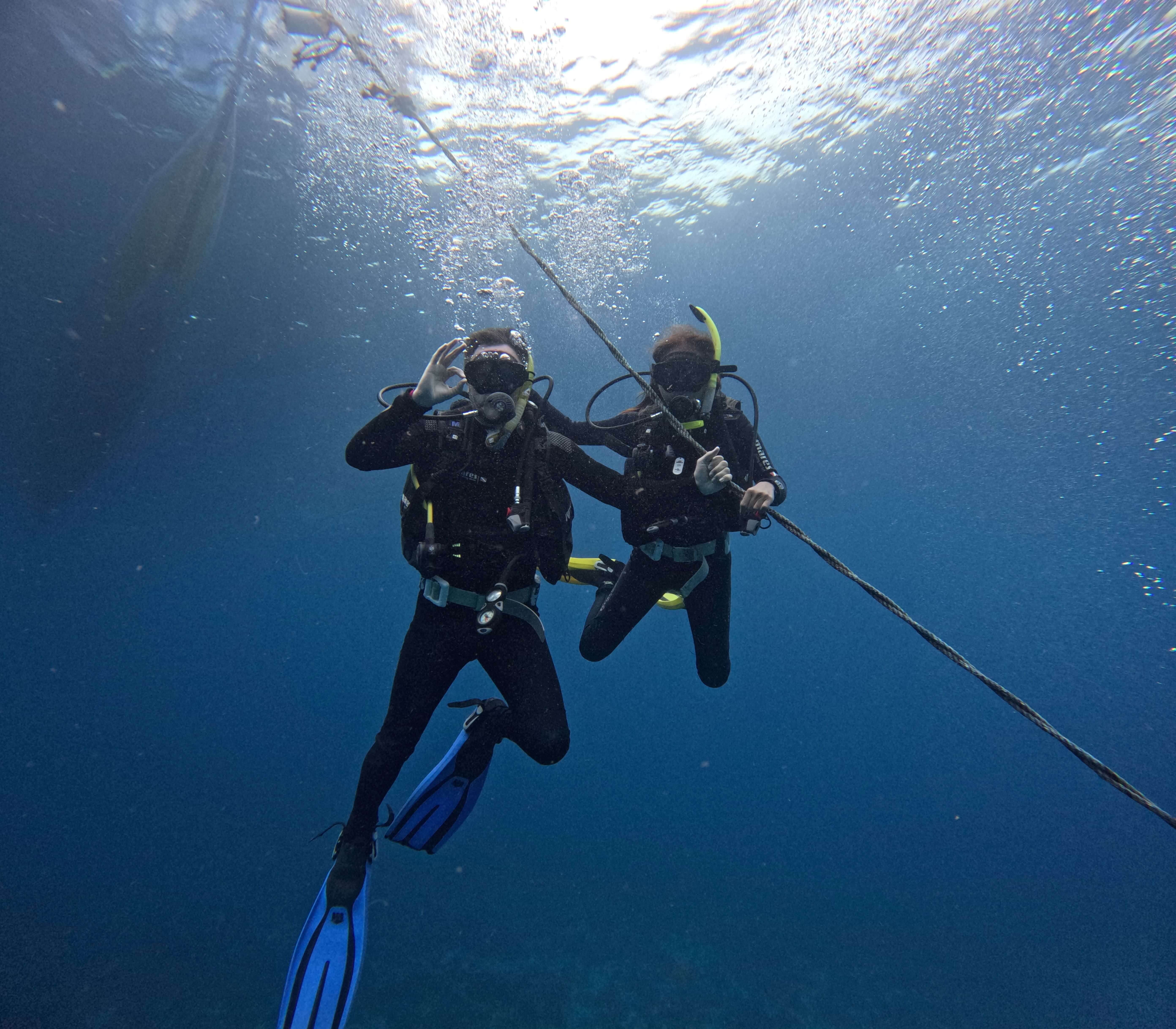 Two scuba divers doing a safety stop holding a rope underwater at Malapascua dive site