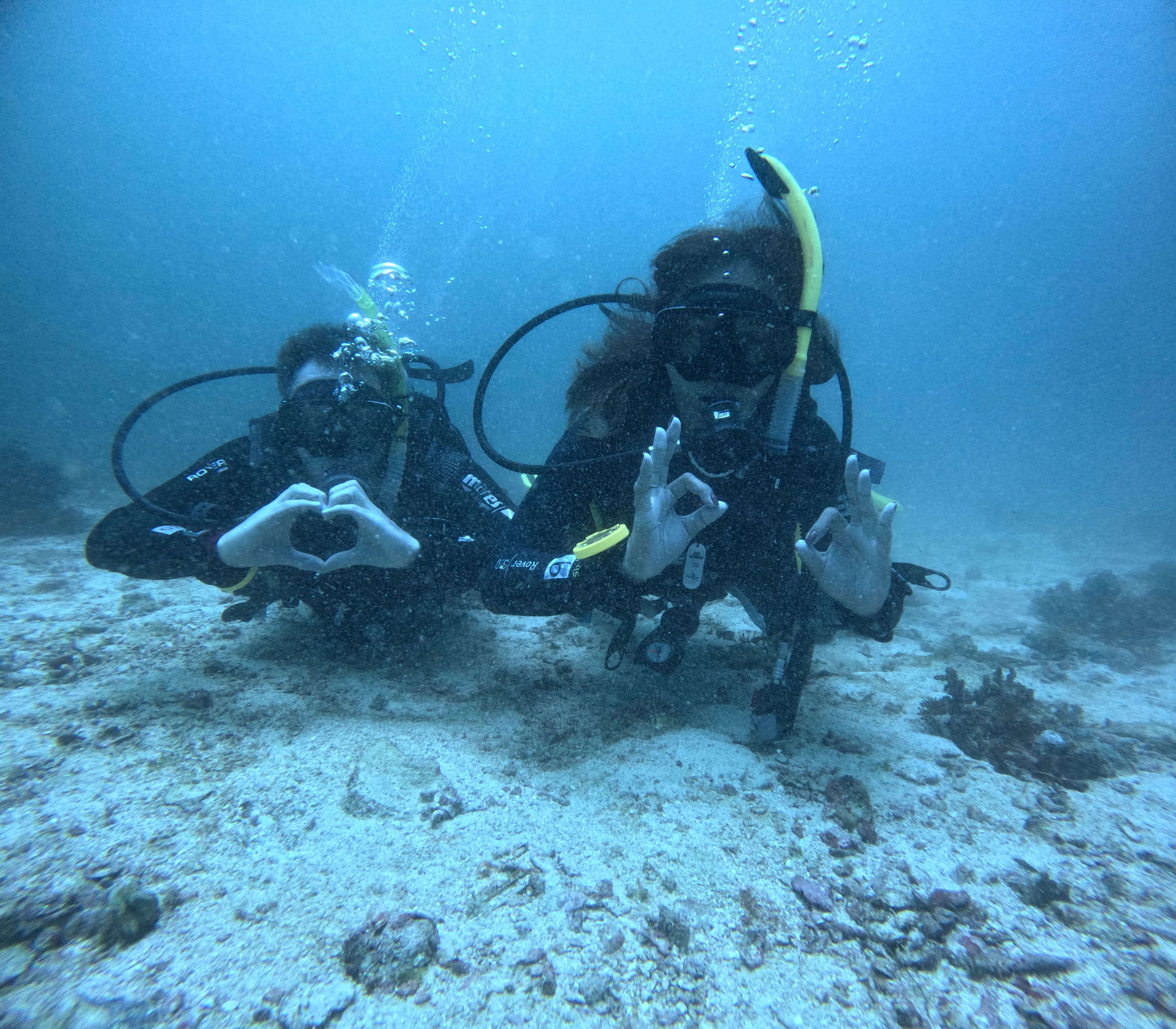 Two scuba divers posing underwater with heart and OK hand signals at Malapascua